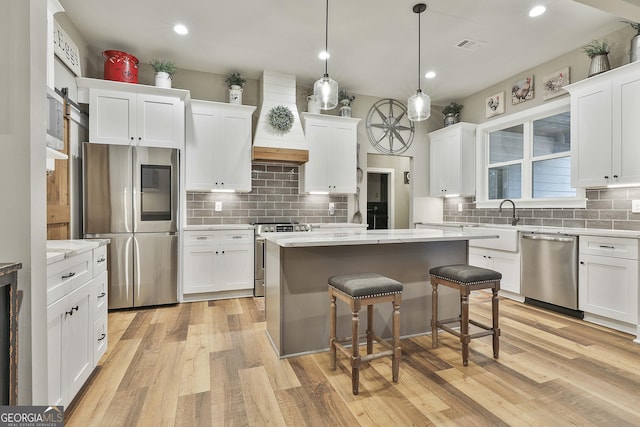 kitchen with stainless steel appliances, custom range hood, white cabinets, a kitchen island, and decorative light fixtures