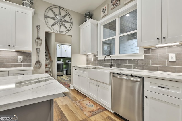 kitchen featuring white cabinetry, sink, stainless steel dishwasher, washing machine and clothes dryer, and light stone countertops