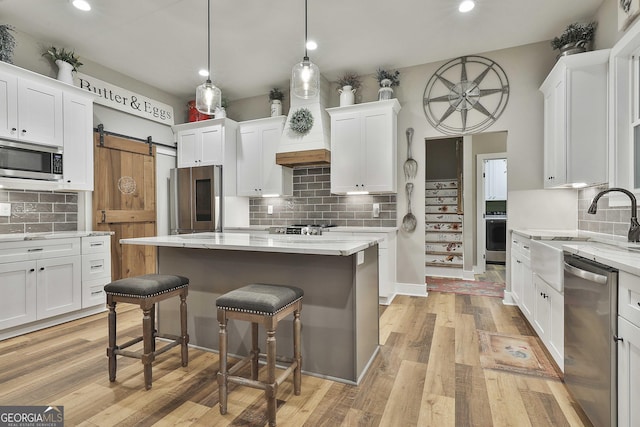 kitchen with a center island, hanging light fixtures, appliances with stainless steel finishes, a barn door, and white cabinets