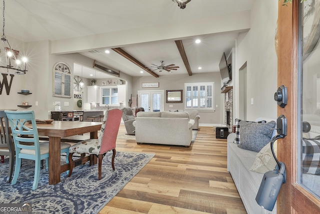 dining space with beam ceiling, ceiling fan with notable chandelier, and light hardwood / wood-style floors