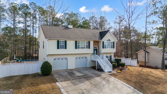 split foyer home with a garage, a shingled roof, concrete driveway, a chimney, and fence