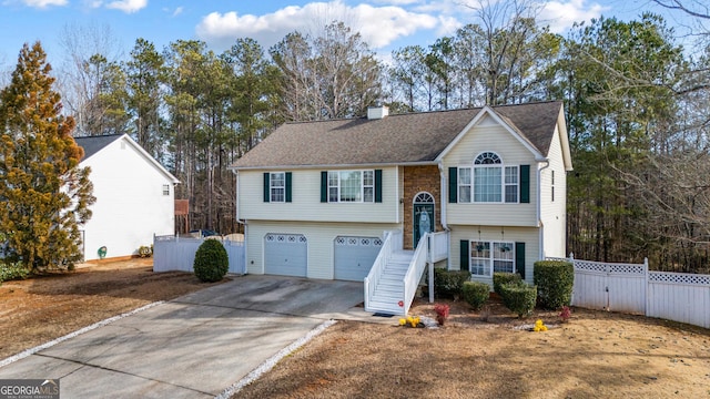 bi-level home featuring an attached garage, fence, driveway, roof with shingles, and a chimney