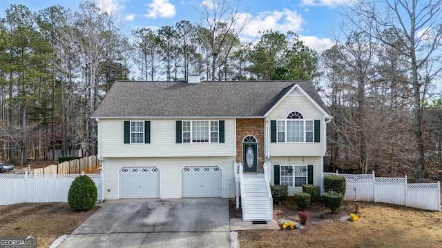 split foyer home featuring a chimney, a shingled roof, fence, a garage, and driveway