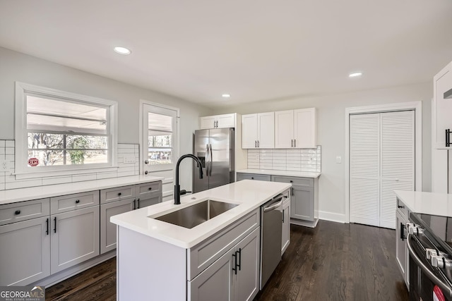 kitchen with sink, appliances with stainless steel finishes, a kitchen island with sink, gray cabinetry, and dark hardwood / wood-style floors