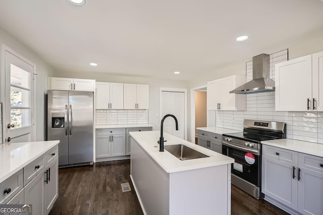 kitchen featuring sink, white cabinetry, a center island with sink, appliances with stainless steel finishes, and wall chimney range hood