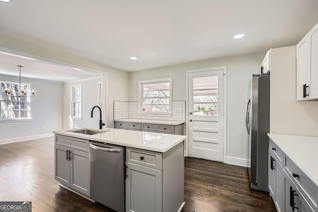 kitchen with sink, gray cabinetry, stainless steel appliances, an island with sink, and decorative light fixtures