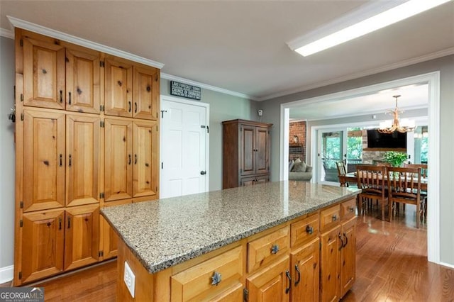 kitchen with a kitchen island, hanging light fixtures, light stone counters, crown molding, and an inviting chandelier