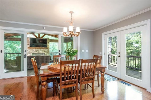 dining area featuring a fireplace, wood-type flooring, a notable chandelier, crown molding, and french doors