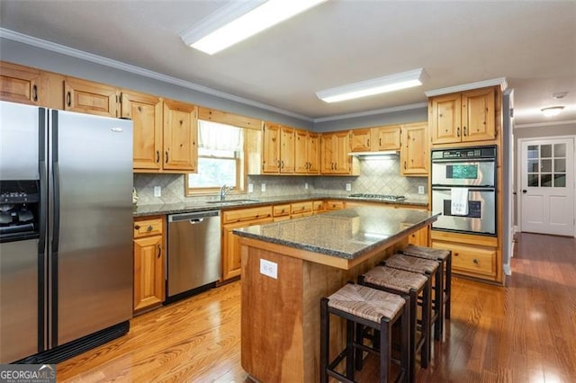 kitchen with sink, crown molding, a kitchen breakfast bar, a kitchen island, and stainless steel appliances