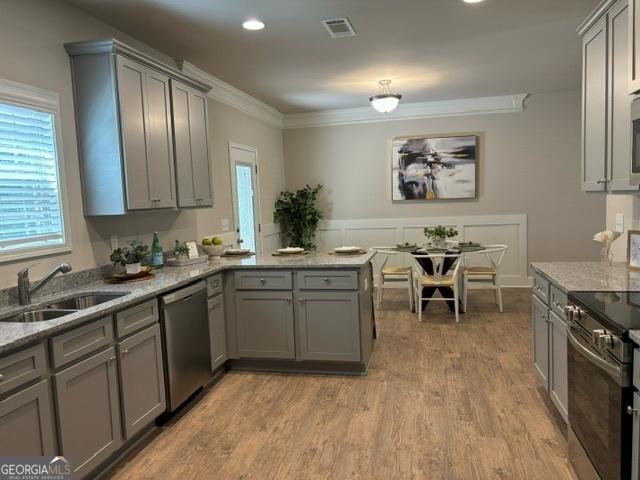 kitchen with appliances with stainless steel finishes, sink, light stone counters, kitchen peninsula, and crown molding