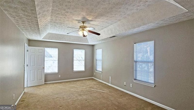 empty room featuring a raised ceiling, ceiling fan, carpet flooring, and a textured ceiling