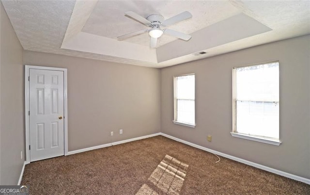 spare room featuring a raised ceiling, ceiling fan, a textured ceiling, and dark carpet