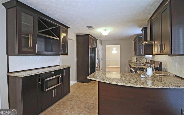 kitchen with light tile patterned floors, light stone counters, tasteful backsplash, a textured ceiling, and kitchen peninsula