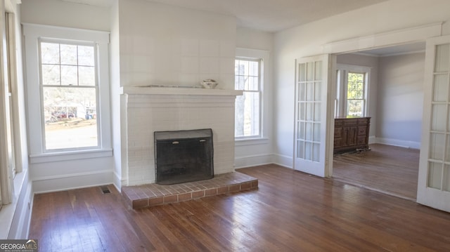 unfurnished living room featuring dark wood-type flooring, a fireplace, french doors, and a wealth of natural light