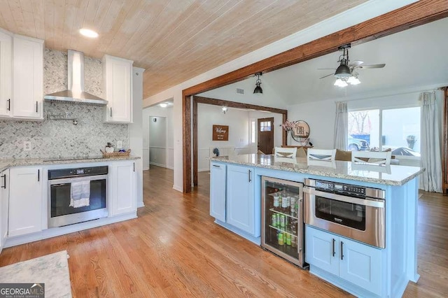 kitchen featuring white cabinetry, stainless steel oven, wall chimney range hood, and wine cooler