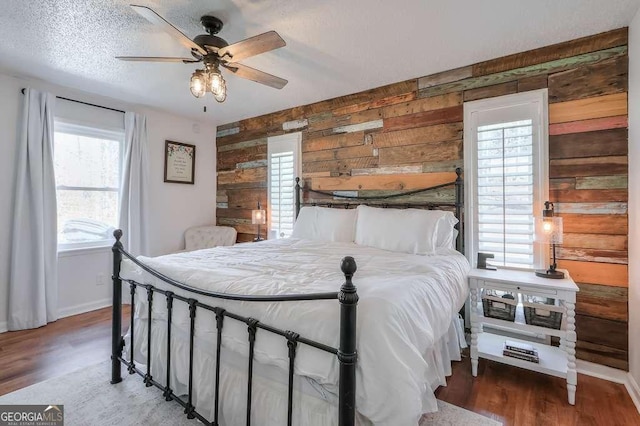 bedroom with hardwood / wood-style flooring, ceiling fan, a textured ceiling, and wooden walls