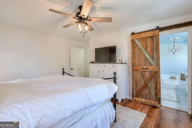 bedroom featuring ceiling fan, wood-type flooring, a barn door, and a textured ceiling