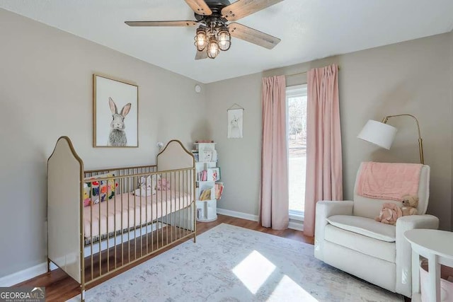 bedroom featuring wood-type flooring, a nursery area, and ceiling fan