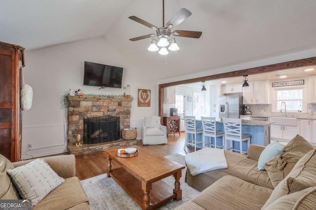 living room with light hardwood / wood-style flooring, a stone fireplace, a wealth of natural light, and vaulted ceiling