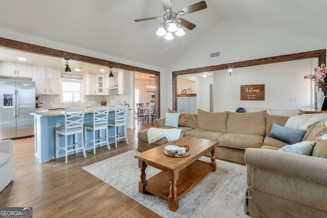 living room featuring ceiling fan, high vaulted ceiling, sink, and light wood-type flooring