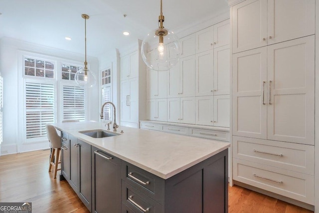 kitchen featuring sink, hanging light fixtures, light hardwood / wood-style flooring, an island with sink, and white cabinets