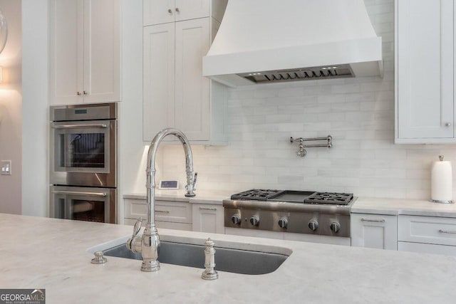 kitchen featuring stainless steel appliances, white cabinetry, custom range hood, and tasteful backsplash