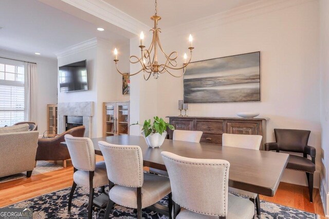 dining room with an inviting chandelier, a high end fireplace, ornamental molding, and light hardwood / wood-style floors