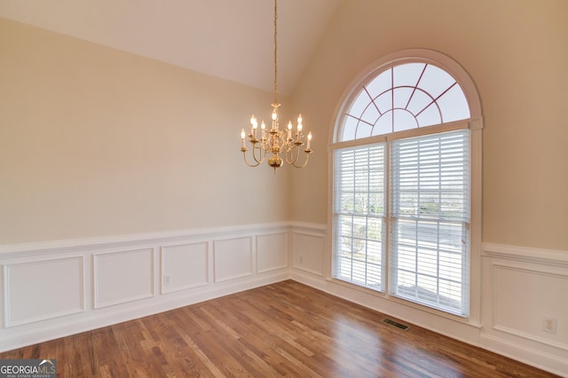 spare room with hardwood / wood-style flooring, vaulted ceiling, and a notable chandelier