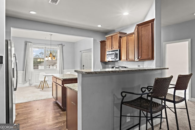 kitchen with dark wood-type flooring, appliances with stainless steel finishes, hanging light fixtures, a kitchen bar, and dark stone counters