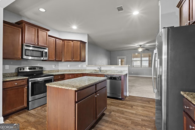 kitchen with a kitchen island, dark hardwood / wood-style floors, sink, light stone counters, and stainless steel appliances