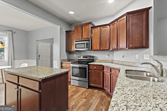 kitchen with sink, light hardwood / wood-style flooring, appliances with stainless steel finishes, light stone countertops, and a kitchen island