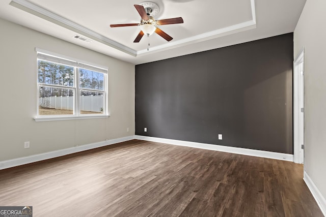 unfurnished room featuring a raised ceiling, hardwood / wood-style floors, and ceiling fan