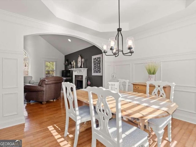 dining space with an inviting chandelier, light hardwood / wood-style flooring, lofted ceiling, and a raised ceiling