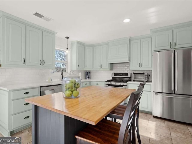 kitchen with hanging light fixtures, stainless steel appliances, a kitchen island, decorative backsplash, and custom exhaust hood