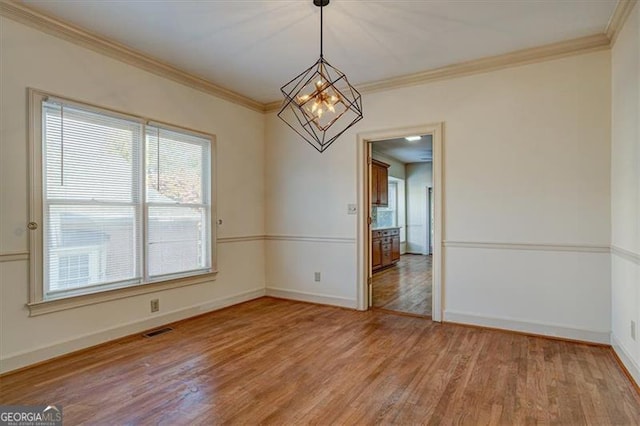 spare room with hardwood / wood-style flooring, ornamental molding, and a notable chandelier