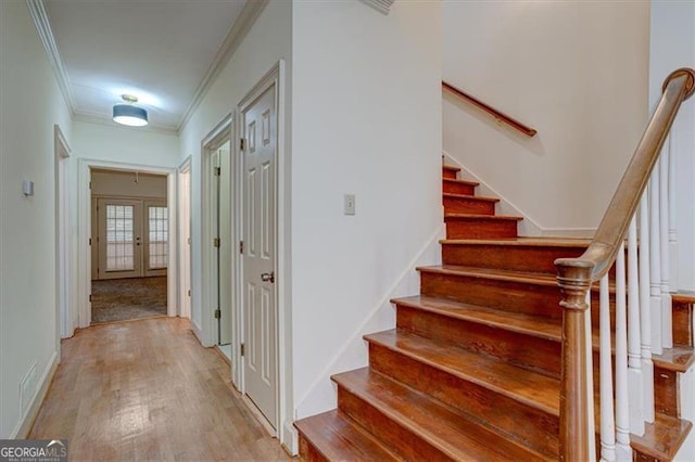 stairway with french doors, ornamental molding, and wood-type flooring