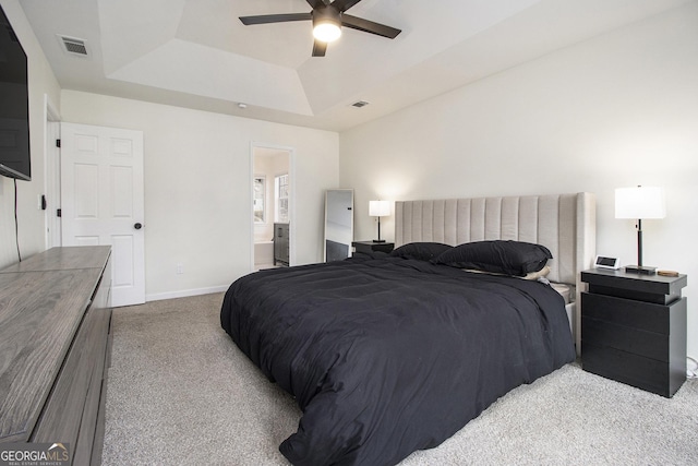 bedroom featuring connected bathroom, light colored carpet, ceiling fan, and a tray ceiling