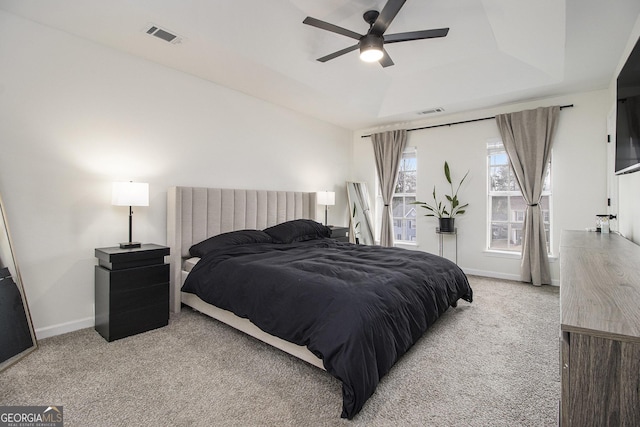 bedroom with a raised ceiling, light colored carpet, and ceiling fan