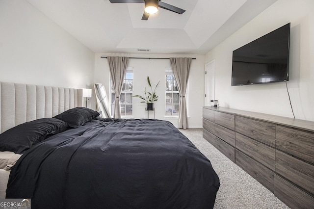 bedroom featuring a tray ceiling, light colored carpet, and ceiling fan