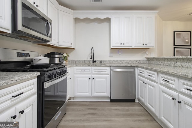 kitchen featuring sink, appliances with stainless steel finishes, light stone countertops, light hardwood / wood-style floors, and white cabinets