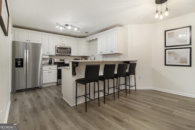 kitchen featuring white cabinets, a kitchen bar, hanging light fixtures, stainless steel appliances, and light stone countertops