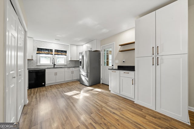 kitchen featuring sink, stainless steel fridge, white cabinetry, black dishwasher, and light wood-type flooring