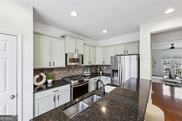 kitchen featuring stainless steel appliances, sink, backsplash, and dark stone counters