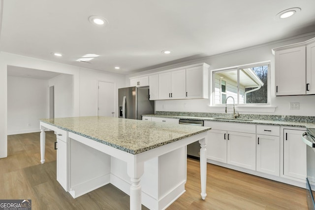 kitchen with sink, white cabinetry, a center island, stainless steel appliances, and light stone countertops