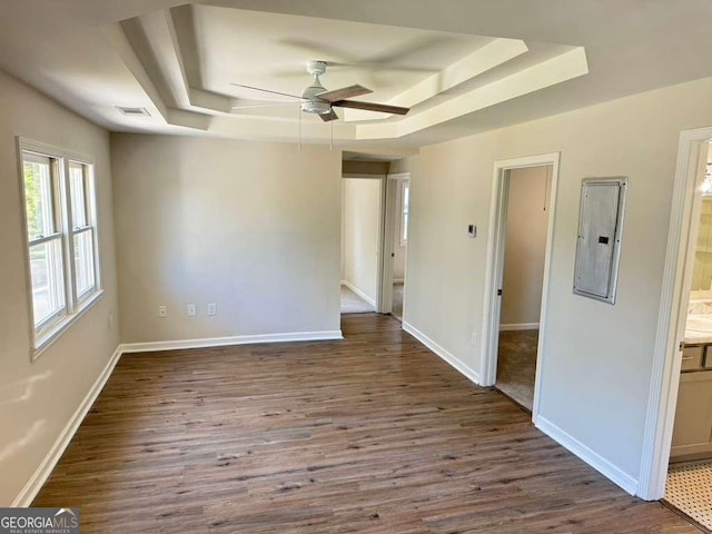 empty room with wood-type flooring, electric panel, ceiling fan, and a tray ceiling