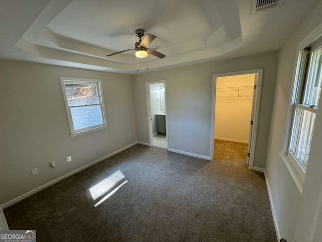 unfurnished bedroom with carpet flooring, connected bathroom, a raised ceiling, a walk in closet, and a closet