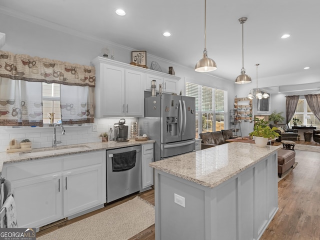 kitchen with appliances with stainless steel finishes, pendant lighting, white cabinetry, sink, and ornamental molding