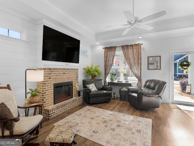 living room with crown molding, ceiling fan, wood-type flooring, and a fireplace