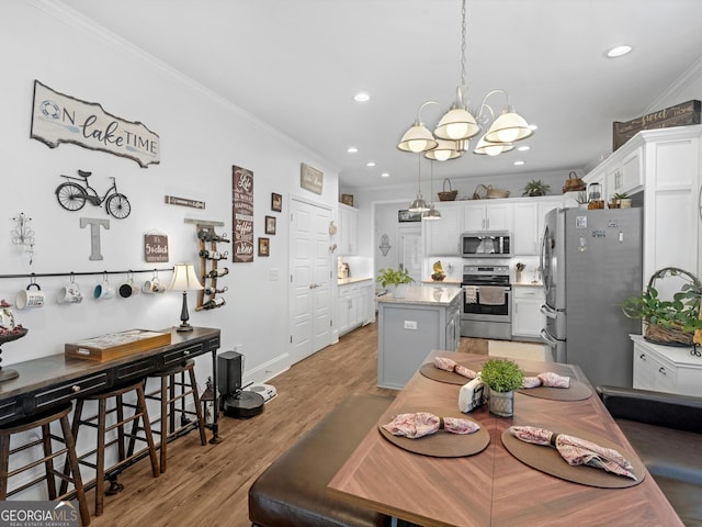 kitchen featuring a kitchen island, appliances with stainless steel finishes, decorative light fixtures, white cabinetry, and crown molding