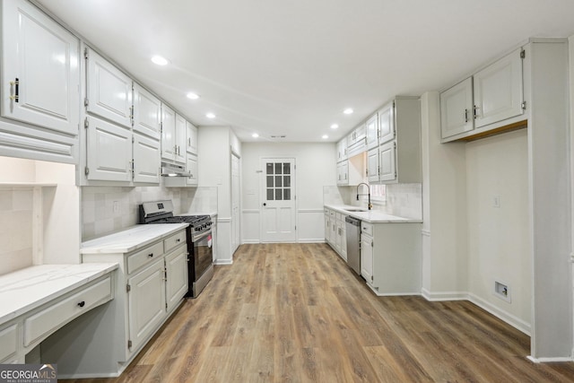 kitchen featuring tasteful backsplash, white cabinetry, sink, stainless steel appliances, and light hardwood / wood-style flooring